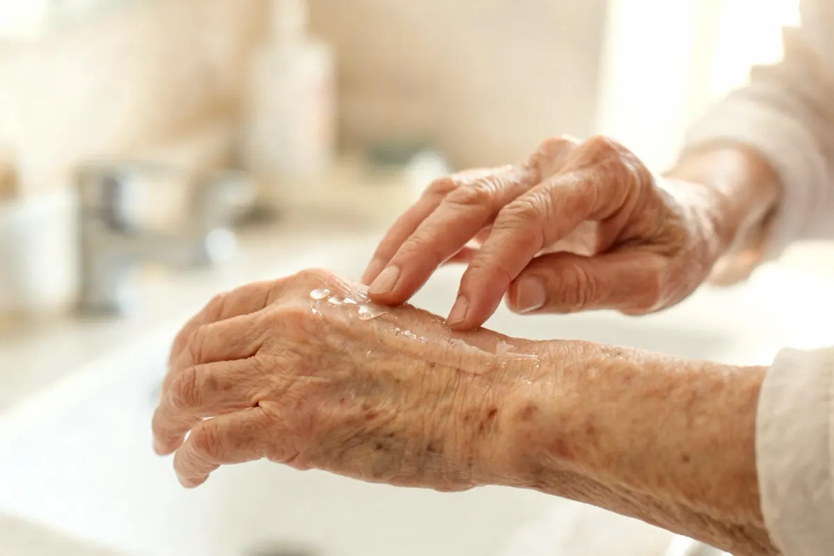 Older woman applying cream to the back of her hand and forearm